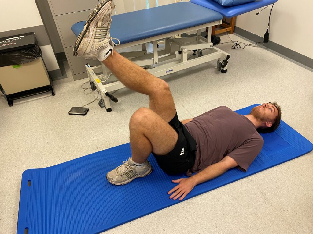 Picture of someone lying on a blue mat on their back with one knee bent and the other leg extended. 