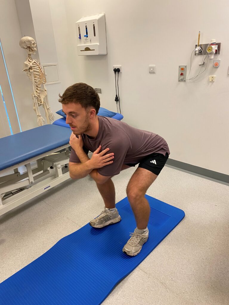 Person squatting on a blue mat with their arms crossed. 