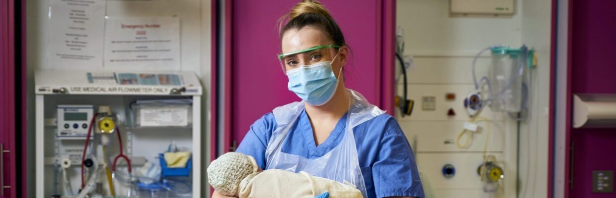 A medical professional wearing PPE holding a baby