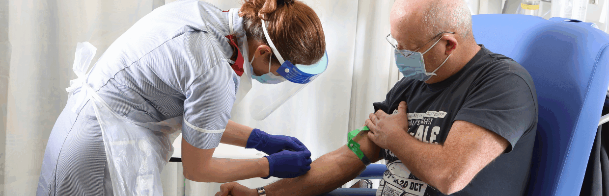 A nurse prepares to draw blood from the arm of a patient sat in a blue chair