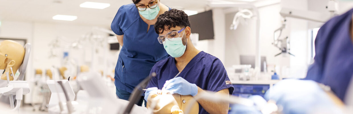 A teacher oversees a dental student working on a simulation model