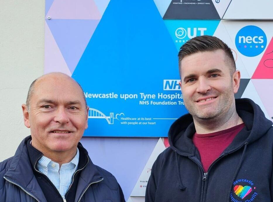 A photo of two men in front of a Newcastle Hospitals sign