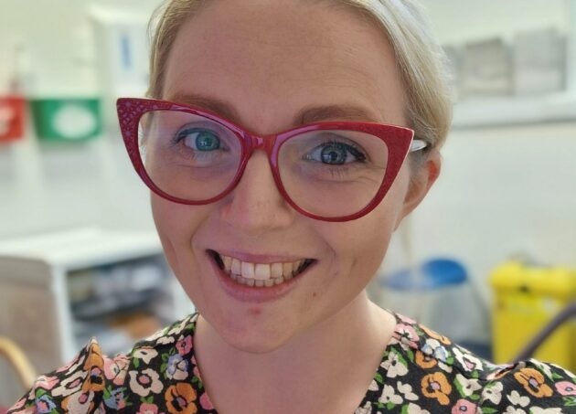 Sophie Whiteway smiling with red glasses and a floral dress.
